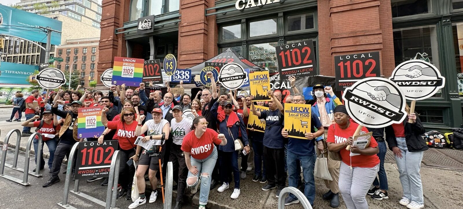 A group of people stand together with union signs in front of an REI store in New York City