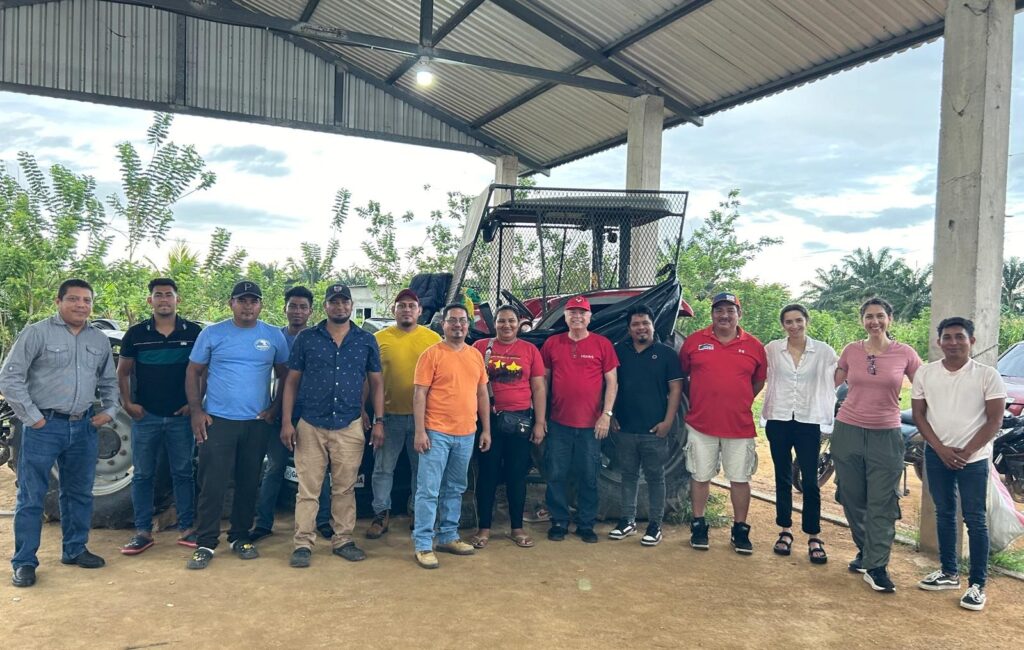 a group of over ten people stand together outside in front of a tractor and farm and smile