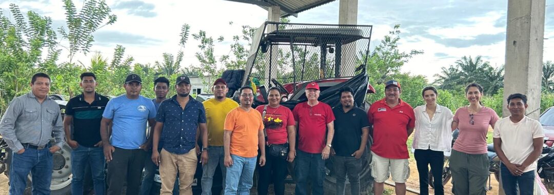 a group of over ten people stand together outside in front of a tractor and farm and smile