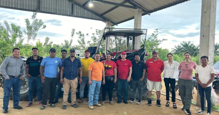 a group of over ten people stand together outside in front of a tractor and farm and smile
