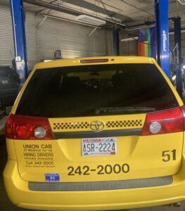 a photo of a taxi cab in a mechanic shop with a rainbow flag hanging behind it 