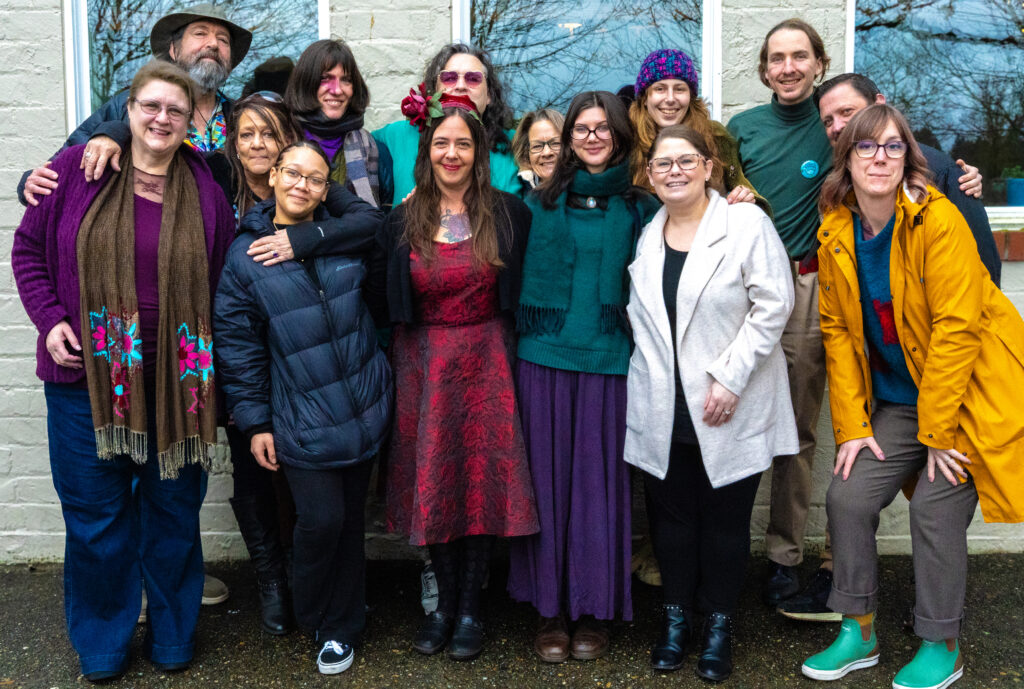 Grupo de 14 personas vestidas en ropa de invierno paran juntas y sonrien. 