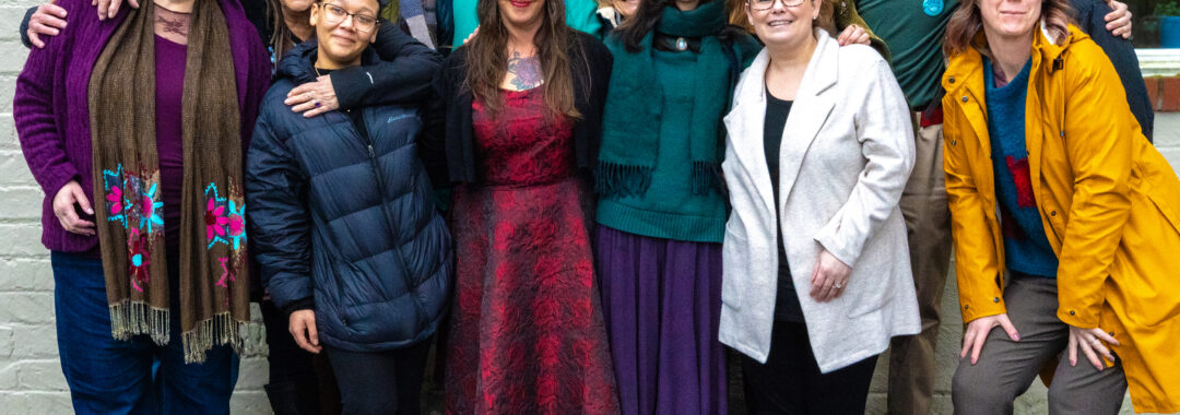 A photo of 14 people wearing winter clothes standing together and smiling.