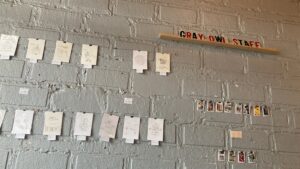 a concrete wall with art strung up and a sign that reads gray owl staff art 