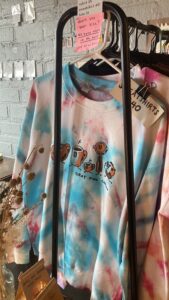 a rack of tie dyed clothing that says gray owl coffee