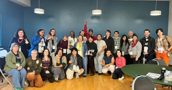 A group photo of over twenty people smiling and standing together in a large room