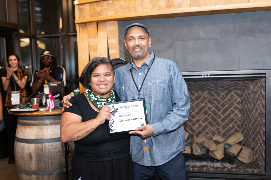 two people standing and smiling together holding an award plaque