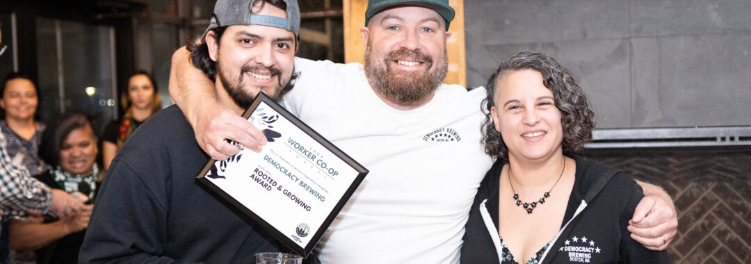 a photo of three people standing and smiling together holding an award plaque