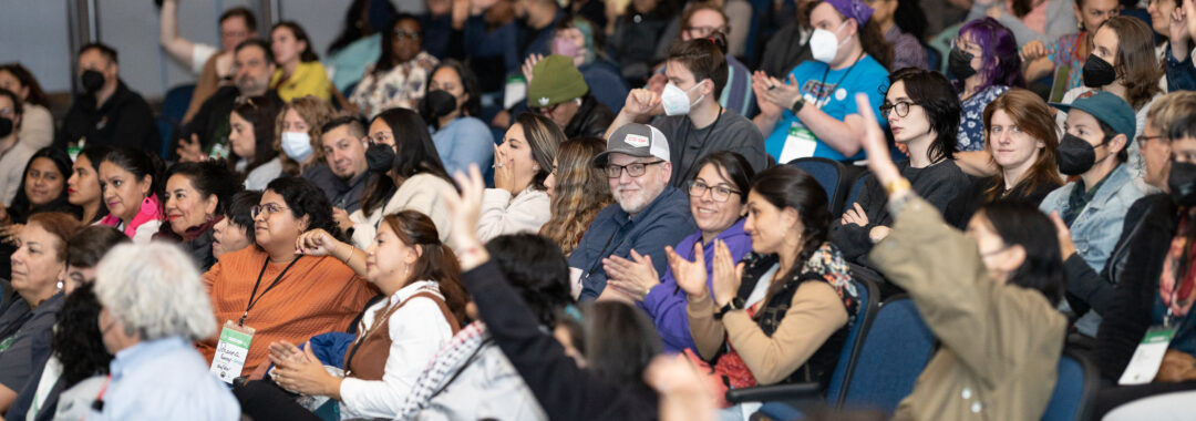 a photo of an audience of people raising their hands and gesturing in an auditorium