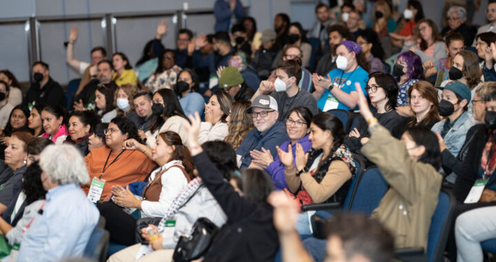 a photo of an audience of people raising their hands and gesturing in an auditorium